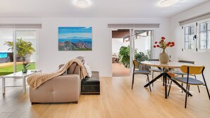 Un amplio salón con un sofá, una mesa de comedor con sillas, un ventanal con vistas y un cuadro en la pared.