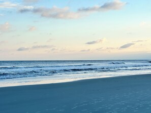 Ein Strand mit Wellen, blauem Himmel und einer entfernten Küstenlinie.