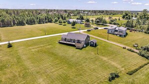 An aerial view of a residential area with houses, a large grassy field, and a road. - Coastal 4BR Getaway w/ Water Views, 2 Min to Brackley Beach (Brackley Beach)