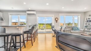 A modern kitchen with a bar area, a dining space with a sofa and chairs, and a balcony with a view. - Coastal 4BR Getaway w/ Water Views, 2 Min to Brackley Beach (Brackley Beach)