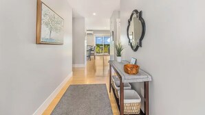 A hallway with a framed artwork, a mirror, a console table with baskets, and a view into a dining area. - Coastal 4BR Getaway w/ Water Views, 2 Min to Brackley Beach (Brackley Beach)
