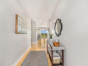 A hallway with a framed artwork, a mirror, a console table with baskets, and a view into a dining area. - Coastal 4BR Getaway w/ Water Views, 2 Min to Brackley Beach (Brackley Beach)