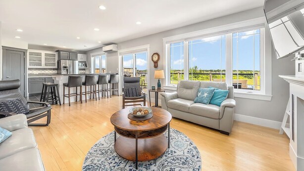 A spacious living area with a kitchen, a round coffee table, and a sofa with a view. - Coastal 4BR Getaway w/ Water Views, 2 Min to Brackley Beach (Brackley Beach)