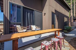 A modern outdoor seating area with a wooden table and chairs, a stone pathway, and a building with large windows and a door. - South Lake Tahoe 2 Bedroom 2 Bath (South Lake Tahoe)