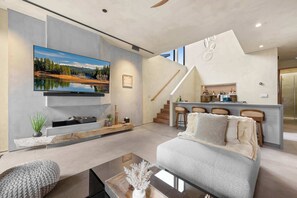 A modern living room with a large flat-screen TV, a sofa, a coffee table, and a kitchen area with bar stools. - Paradise South Lake Tahoe 3 Bedroom 3 Bath (South Lake Tahoe)
