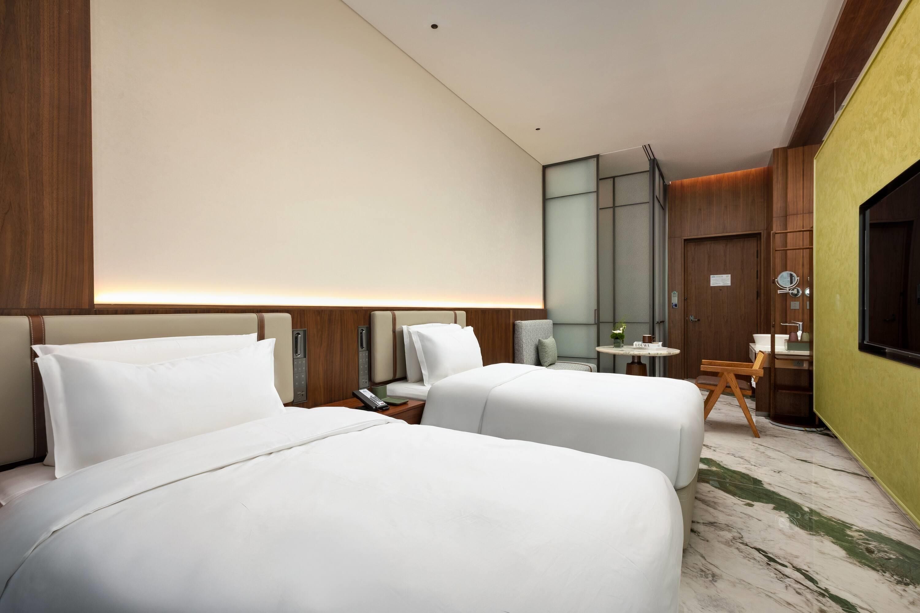 A hotel room with two beds, a small table, a chair, a mirror, and a TV.