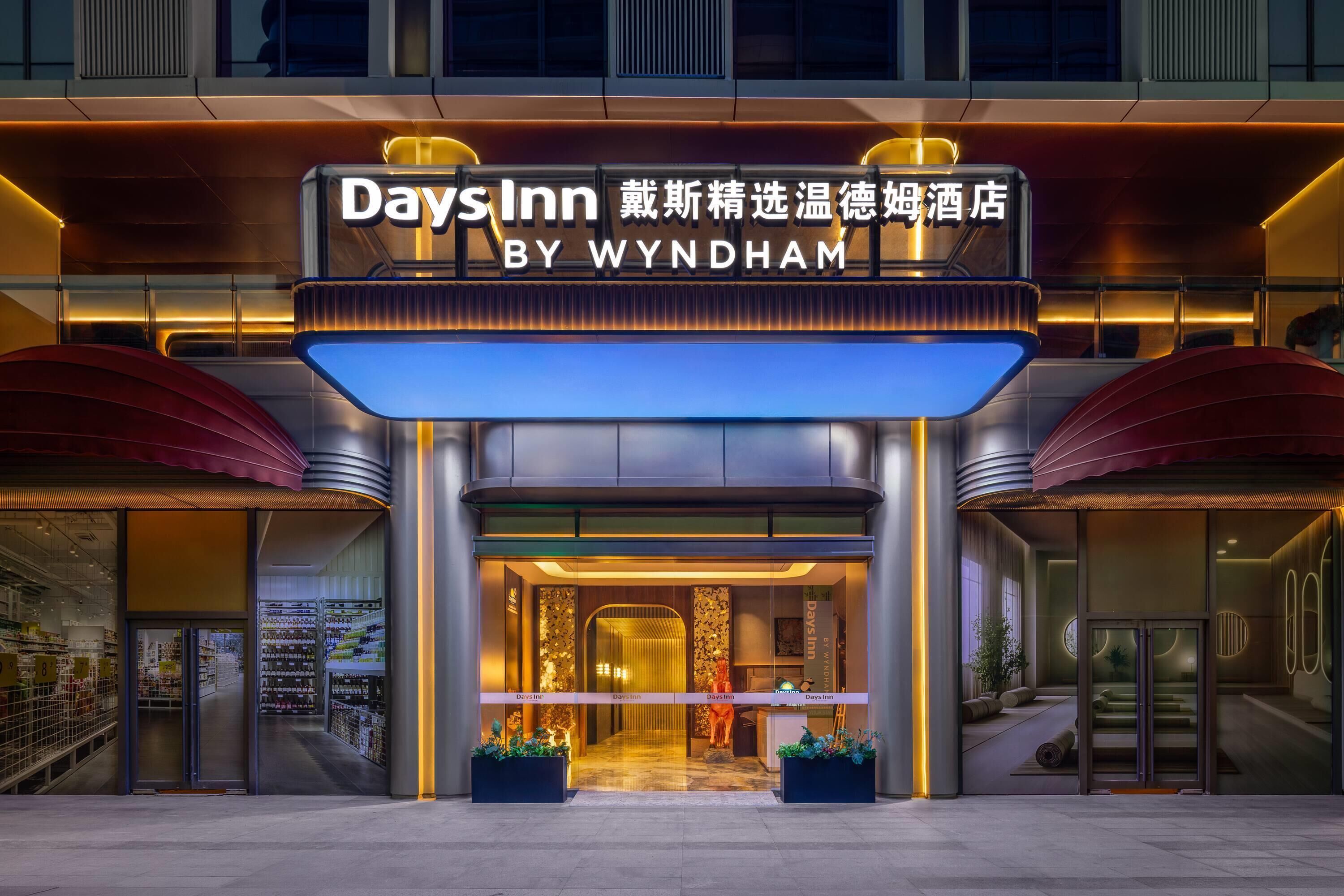 A hotel entrance with a sign reading 'Days Inn BY WYNDHAM' and a modern design with a glass facade and a red awning.
