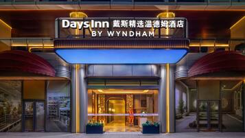 Een hotelingang met een bord waarop 'Days Inn BY WYNDHAM' staat, uitgevoerd in een modern design met een glazen gevel en een rode luifel.