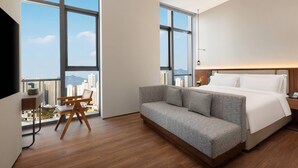 Moderni hotellihuone, jossa on suuri ikkuna, sohva, työpöytä ja sänky.