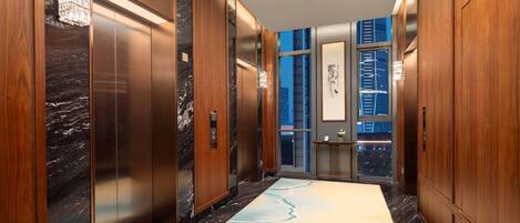 A modern elevator with wood paneling and marble accents, leading to a lobby with a marble floor and a cityscape view.