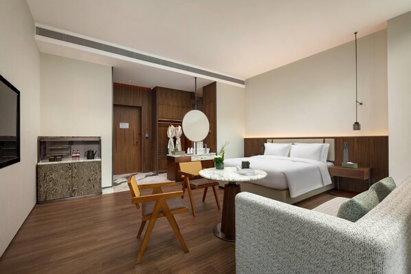 Une chambre d’hôtel comprenant un lit, une table à manger avec des chaises, un canapé, un petit coin cuisine et un miroir.