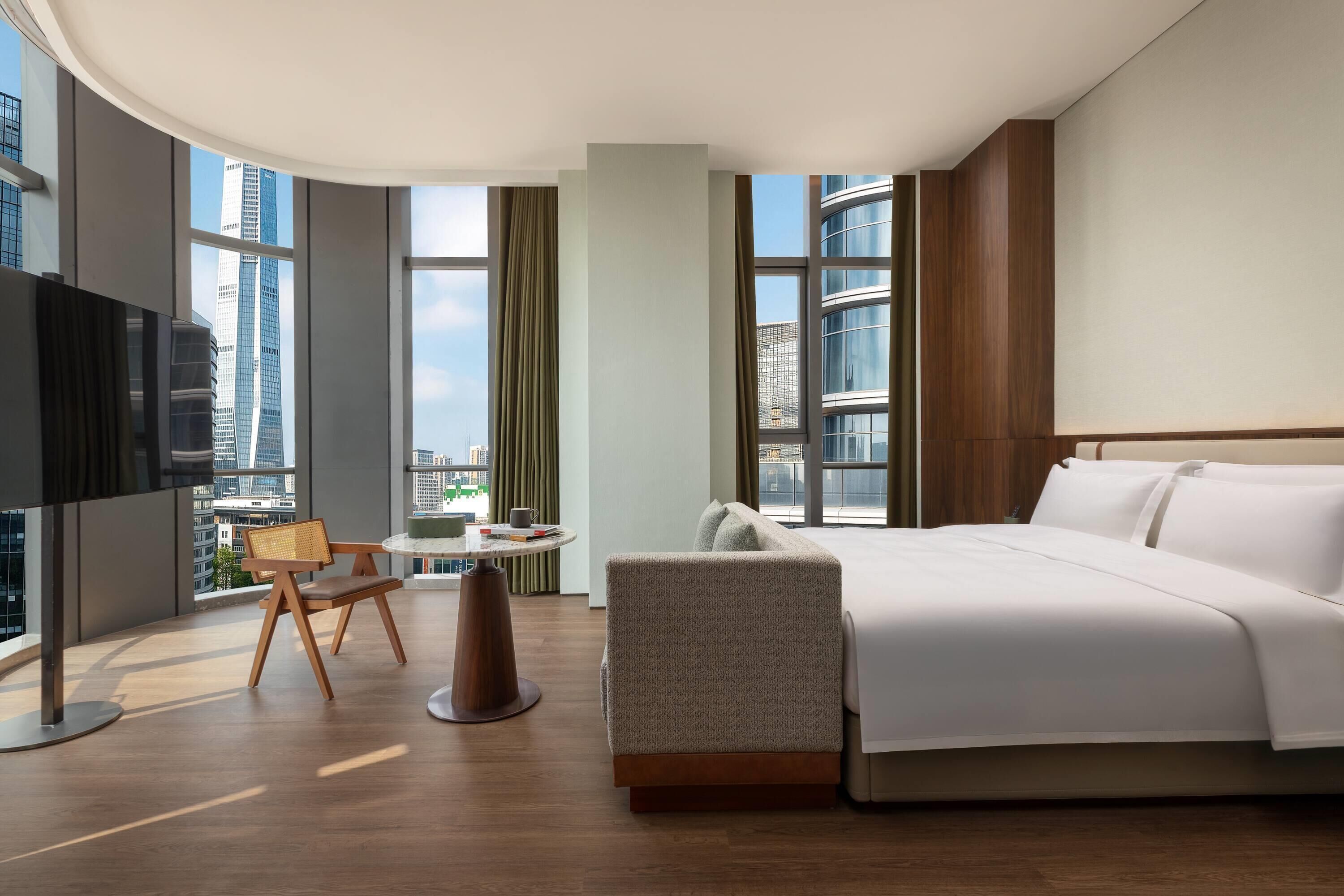 A hotel room with a bed, a TV, a round table, and a chair.