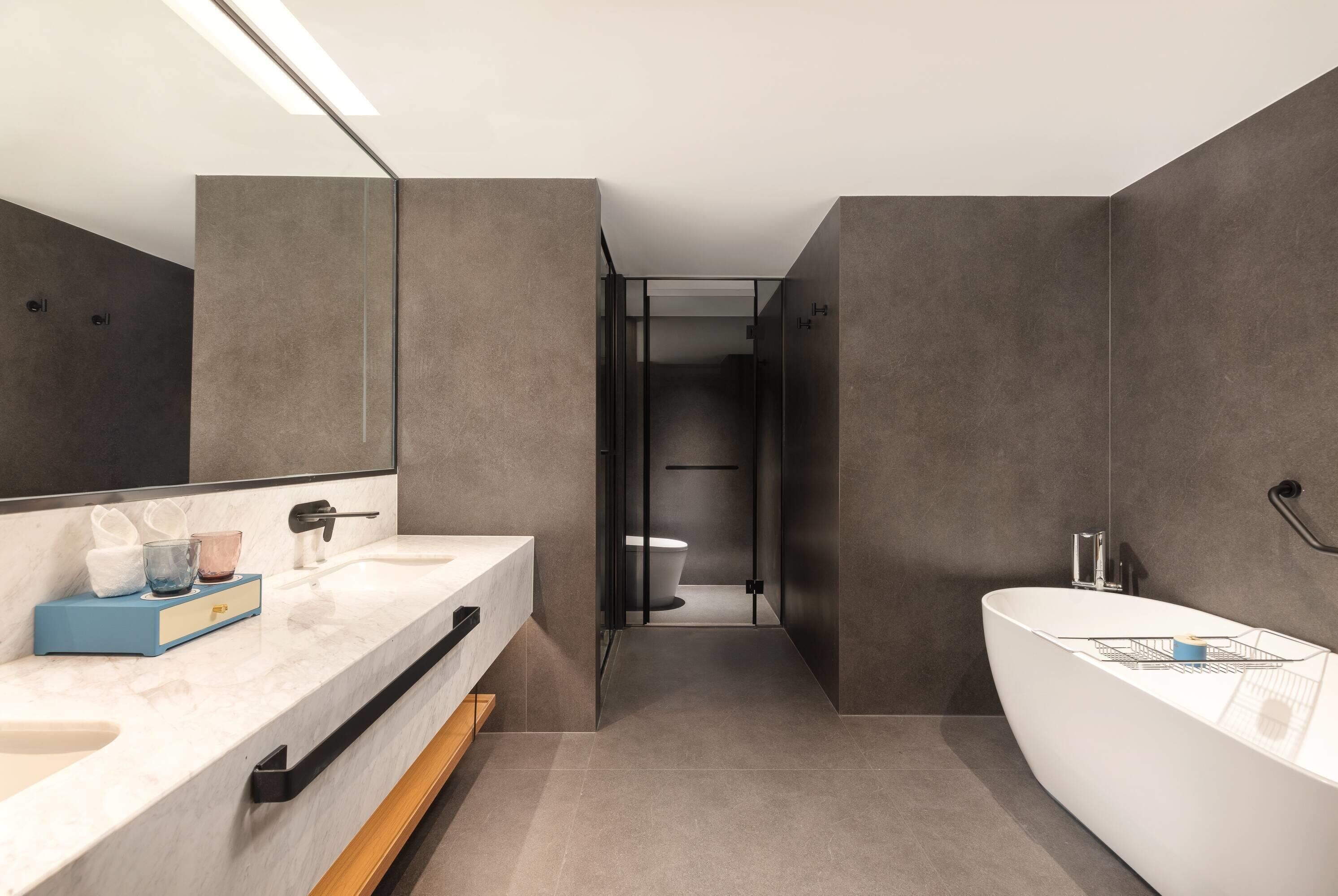A modern bathroom with a large mirror, a white bathtub, and a separate toilet area.