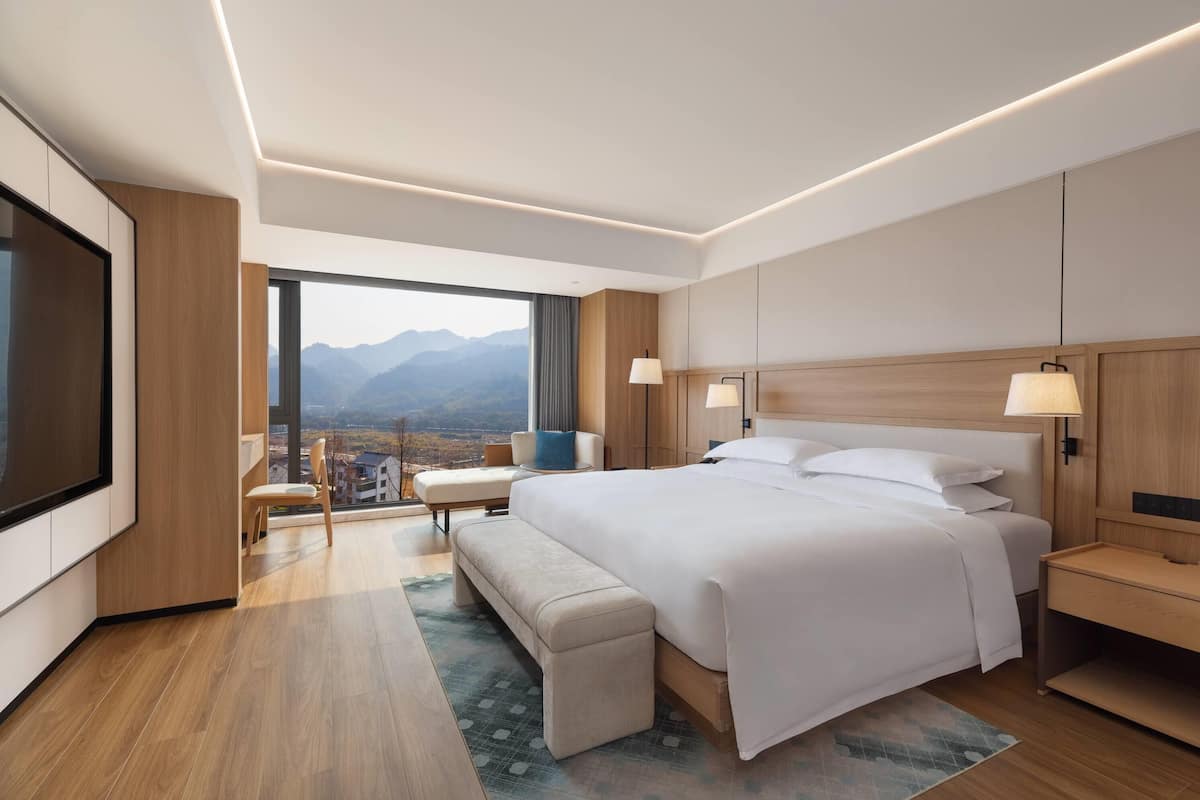 Een moderne hotelkamer met een groot bed, een zithoek, een televisie en uitzicht op bergen.