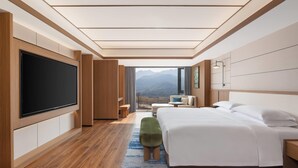 A modern hotel room with a large flat-screen TV, a bed, a seating area, and a view of mountains. - Days Hotel By Wyndham Lishui Liandu (Lishui)
