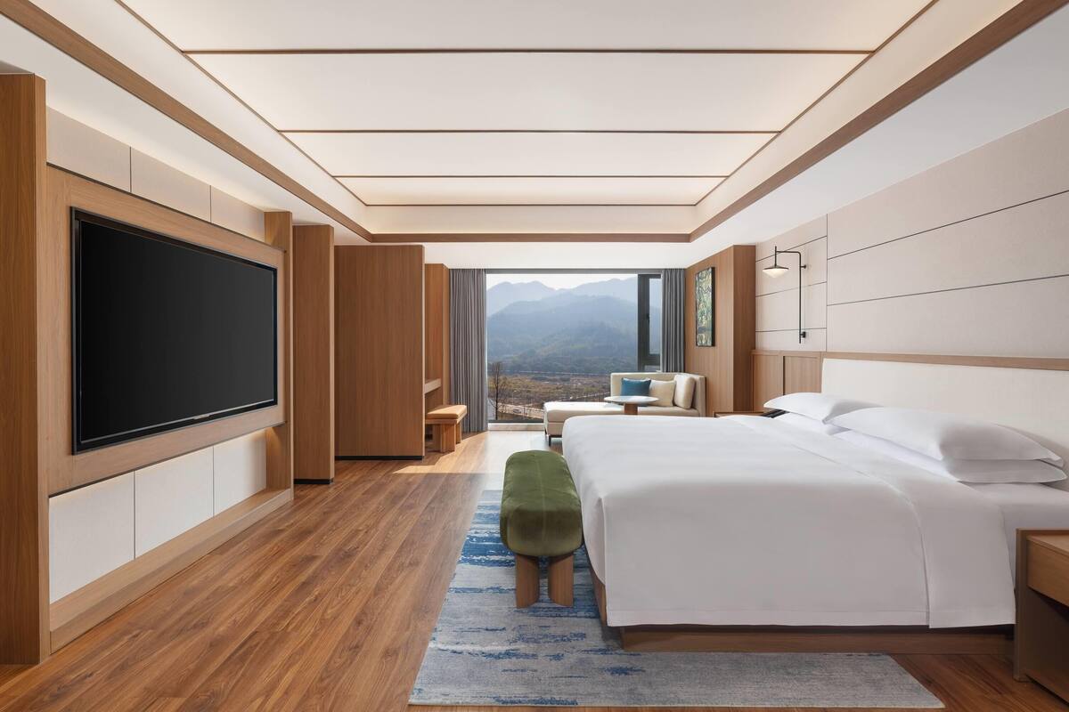 Een moderne hotelkamer met een grote flatscreen-tv, een bed, een zithoek en uitzicht op bergen.