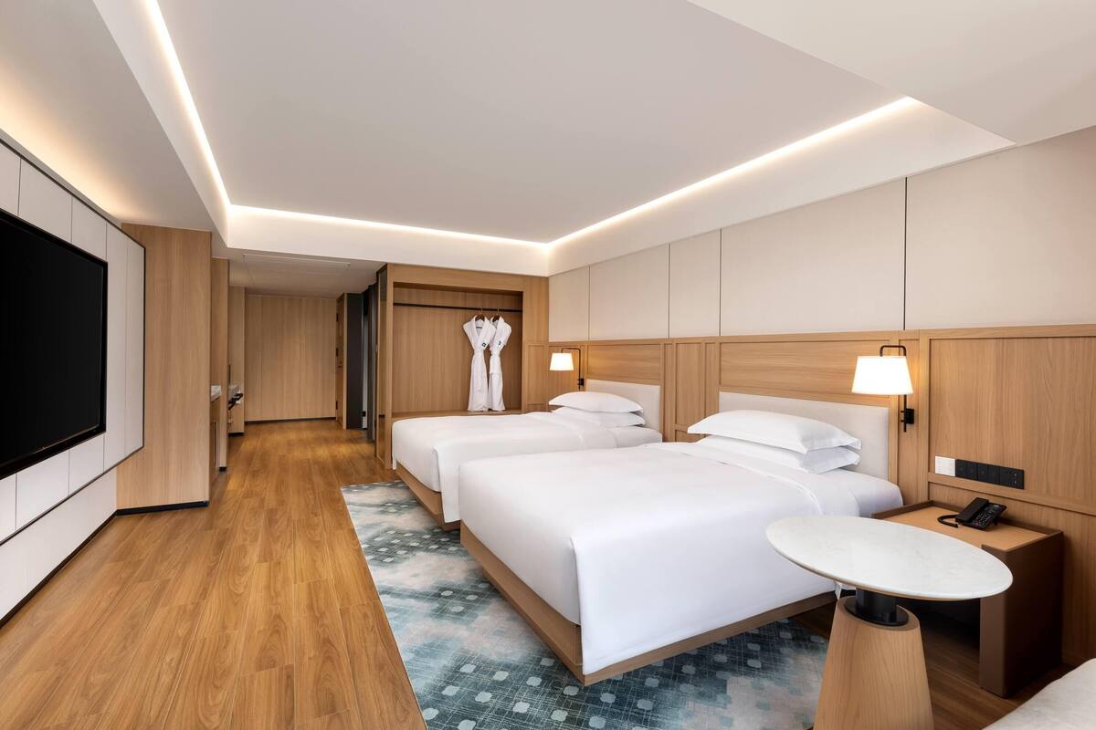 Een hotelkamer met twee bedden, een bureau, een televisie en een kledingkast voor jassen.