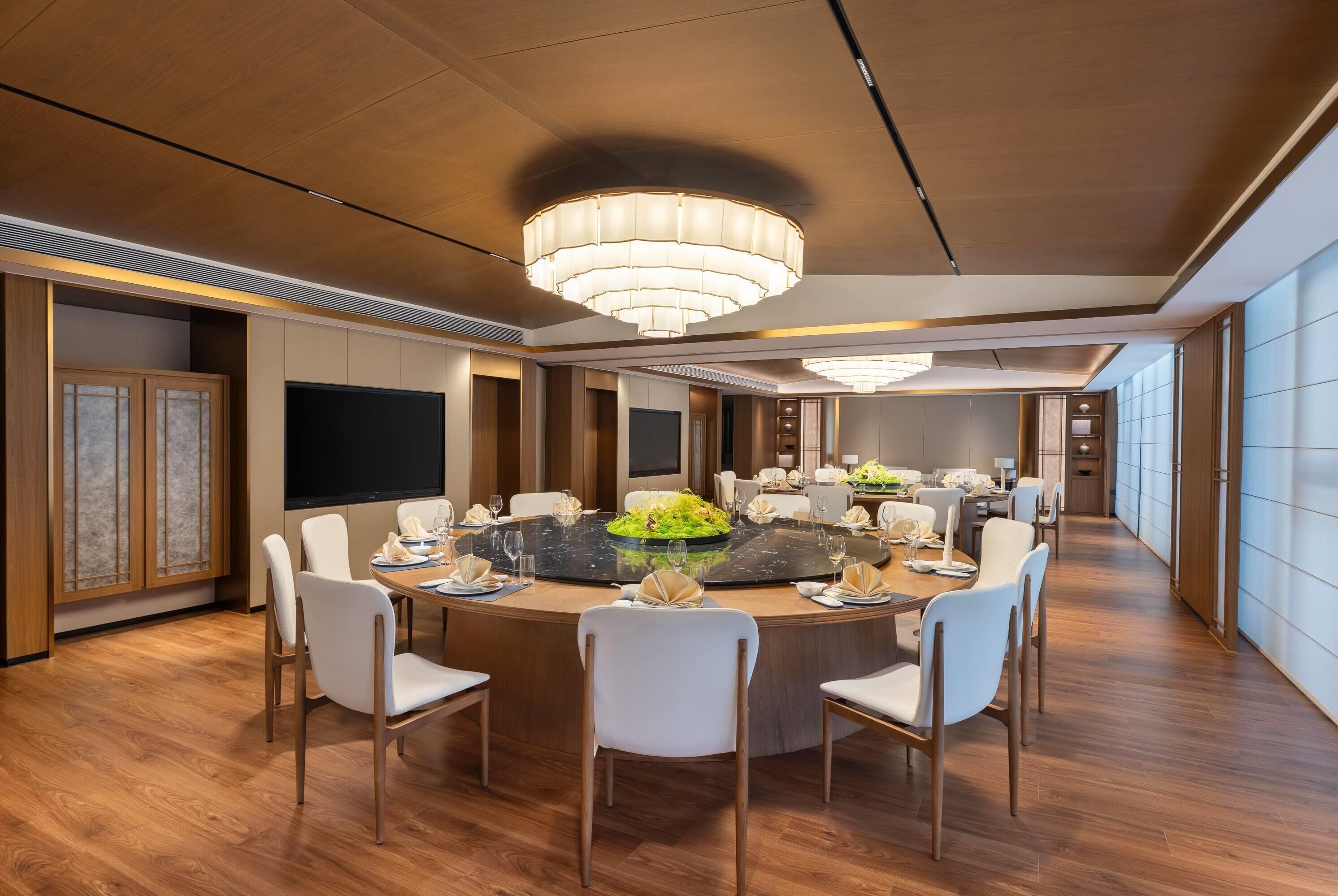 A modern dining area with a round table, white chairs, and a chandelier.