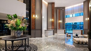 Eine moderne Lobby mit Marmorboden, einer Rezeption, einer Sitzecke und großen Fenstern.