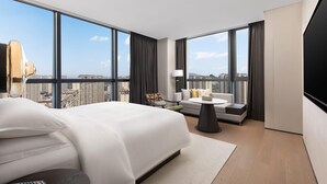 Ein modernes Hotelzimmer mit einem großen Bett, einer Sitzecke, einem Fernseher und Blick auf die Stadt.