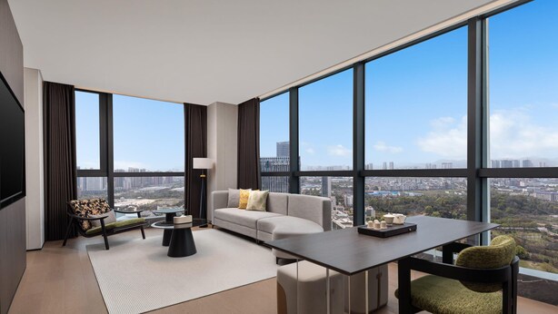 Ein modernes Wohnzimmer mit einer Couch, einem Esstisch und Blick auf eine Stadtlandschaft durch große Fenster.