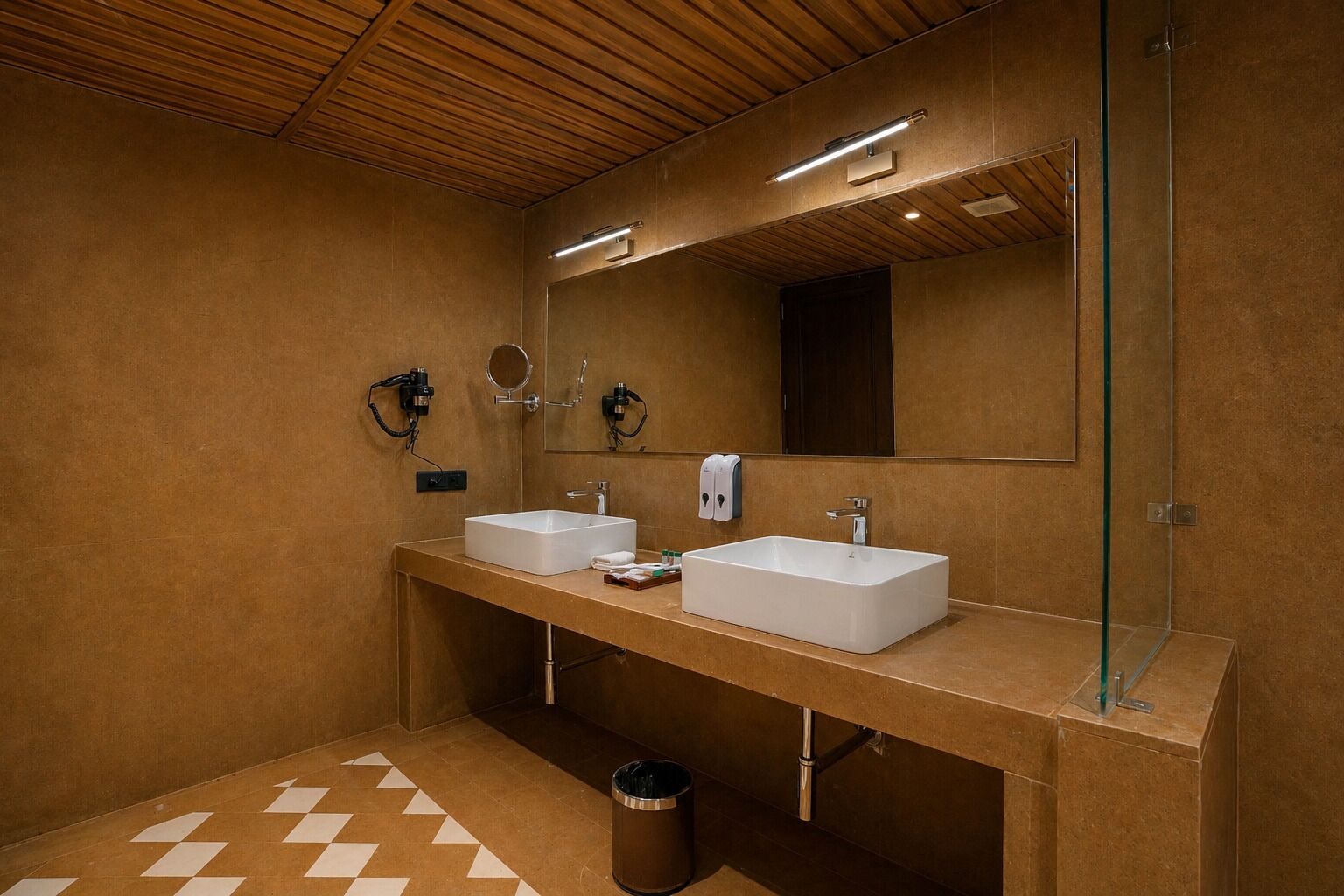 A modern bathroom with two sinks, a mirror, and a trash bin.