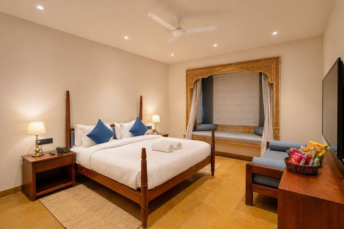 Una habitació d'hotel amb llit, taules de nit, escriptori, cadira, televisió i finestra amb cortines.