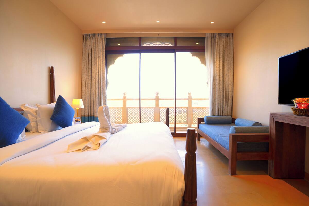Habitació d'hotel amb llit, sofà, televisió i balcó amb cortines.