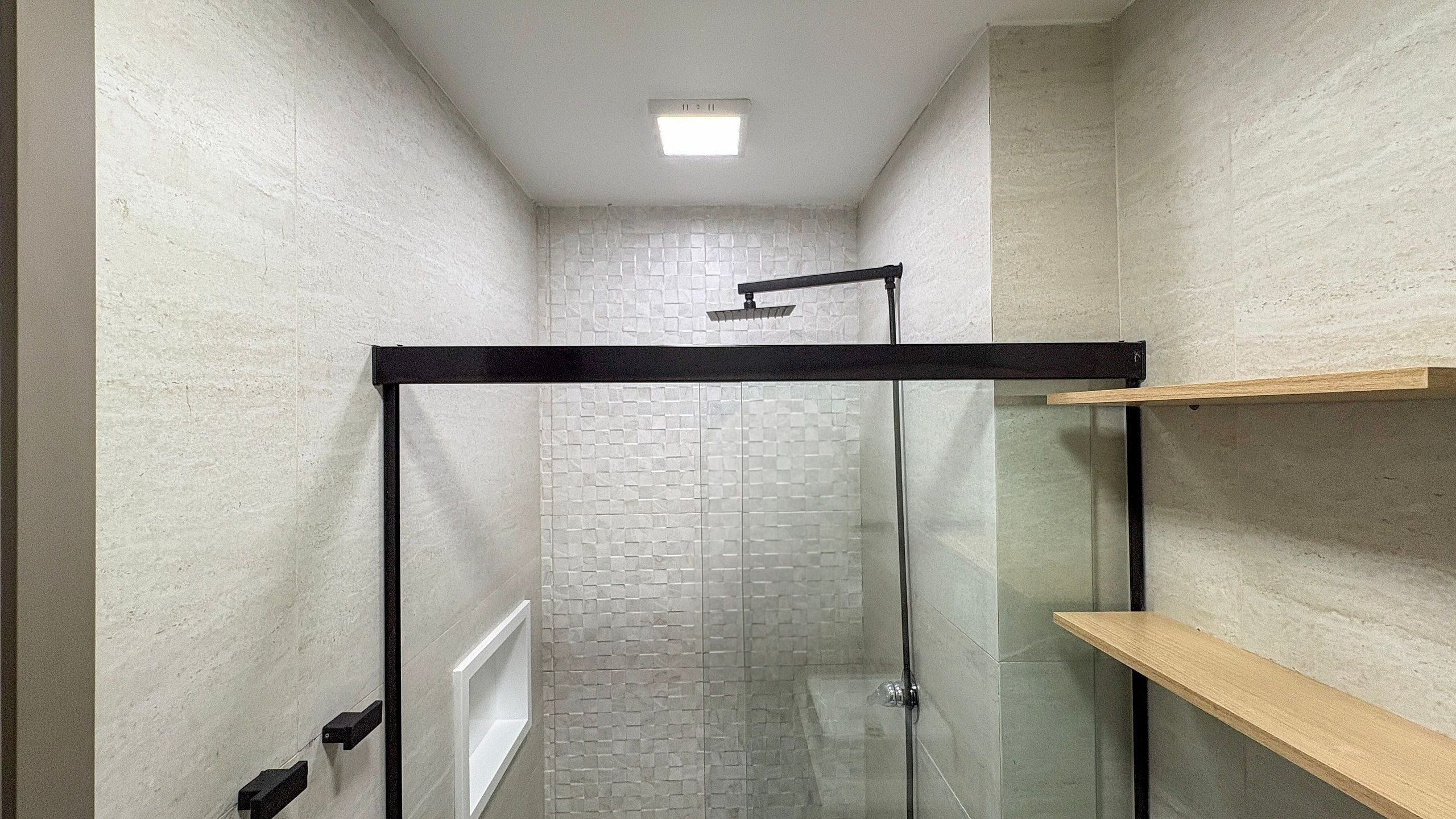 A narrow hallway with a glass shower enclosure and a wooden shelf.