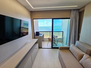 A modern hotel room with a flat-screen TV, a sofa, a dining area with a table and chairs, and a balcony with a view of the sea. - Prime Beach Tamandaré (Tamandaré)