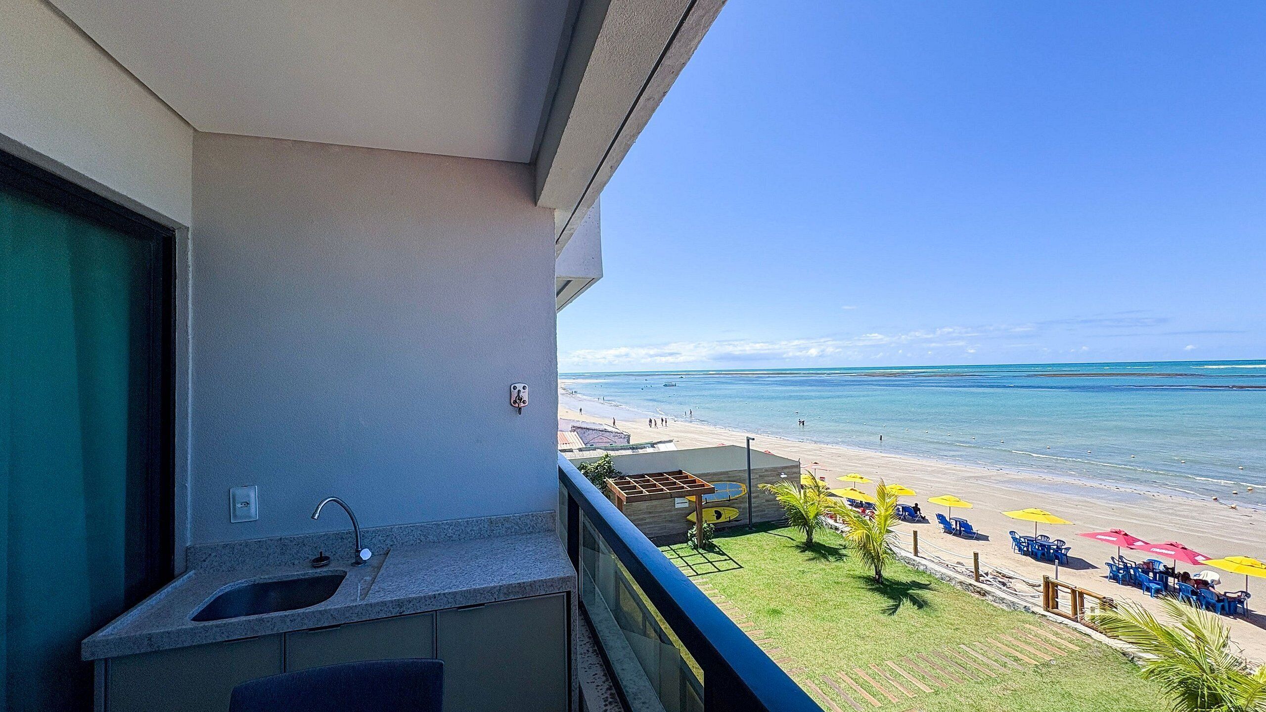 Un balcon équipé d’un évier et offrant une vue sur une plage avec des parasols et des chaises longues.