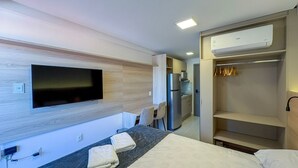 Ein Hotelzimmer mit Bett, Schreibtisch, Flachbildfernseher, Küchenzeile und begehbarem Kleiderschrank.