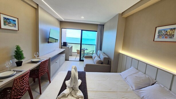 Ein Hotelzimmer mit Bett, Schreibtisch, Stuhl, einer kleinen Pflanze und Meerblick.