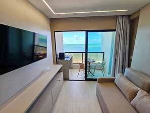 A modern hotel room with a flat-screen TV, a sofa, a dining area with a table and chairs, and a balcony with a view of the sea. - Prime Beach Tamandaré (Tamandaré)