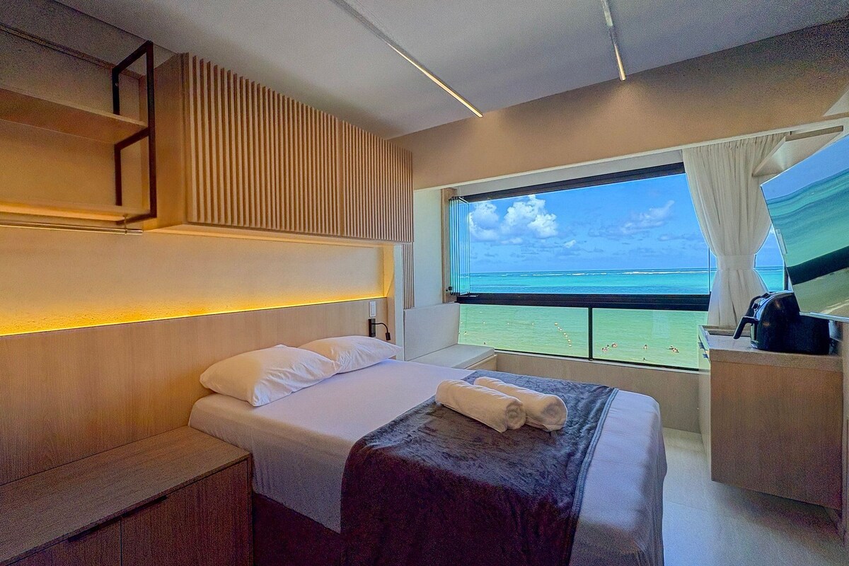 A modern hotel room with a bed, a seating area, and a large window with a view of the ocean.