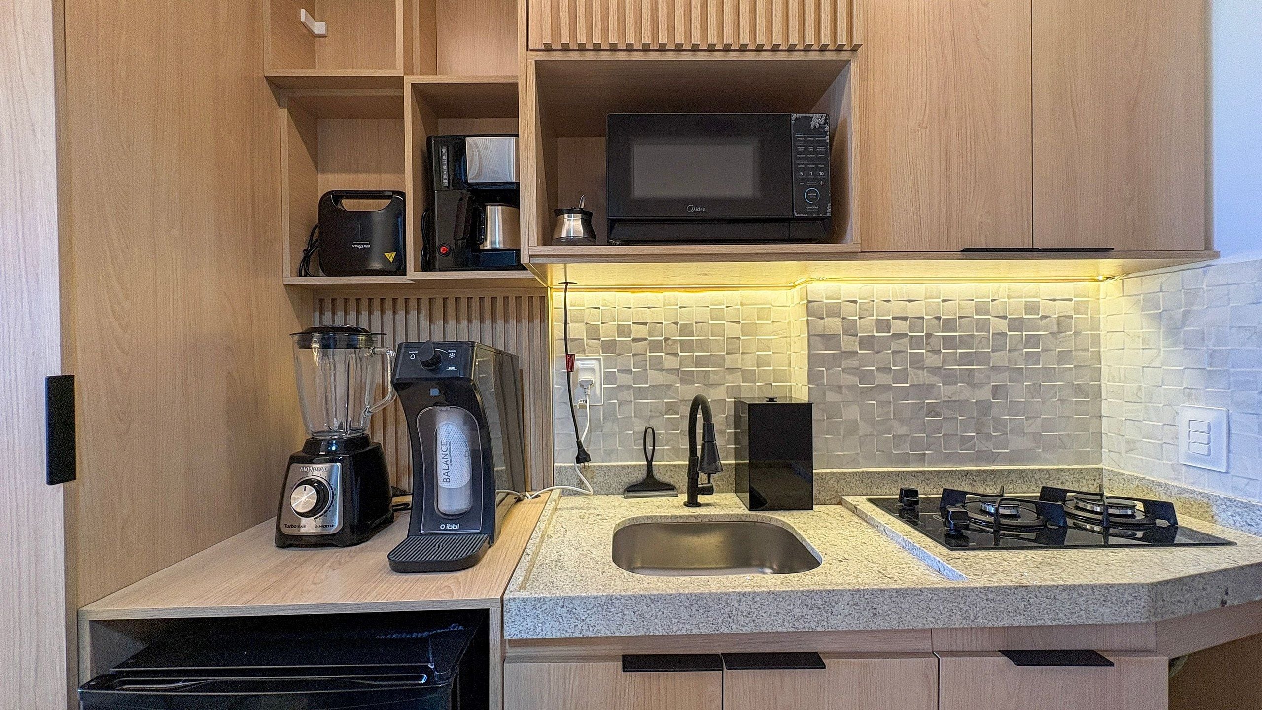 A compact kitchen with a built-in microwave, a coffee maker, a blender, and a gas stove.