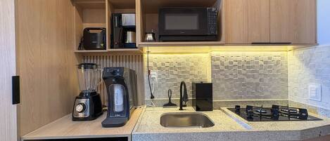 A compact kitchen with a built-in microwave, a coffee maker, a blender, and a gas stove.