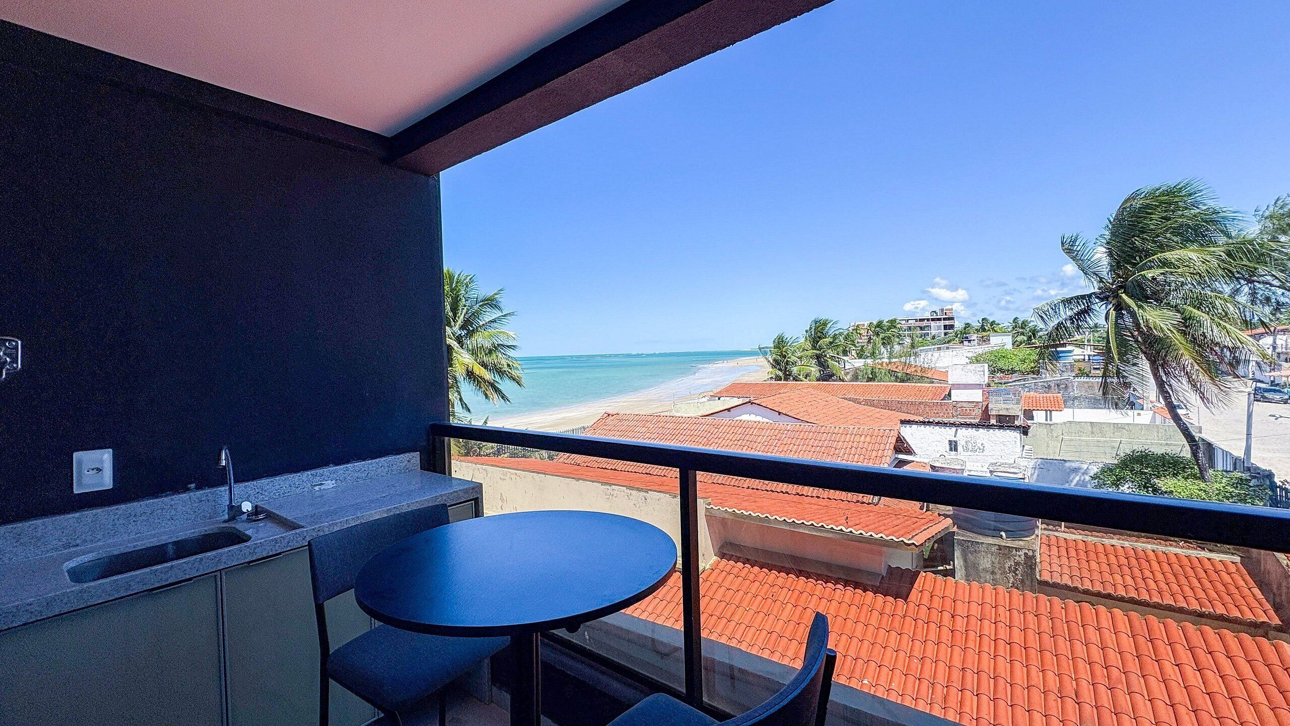 A balcony with a view of the beach, a table, and a chair.