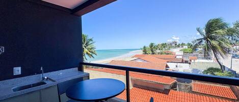 A balcony with a view of the beach, a table, and a chair.