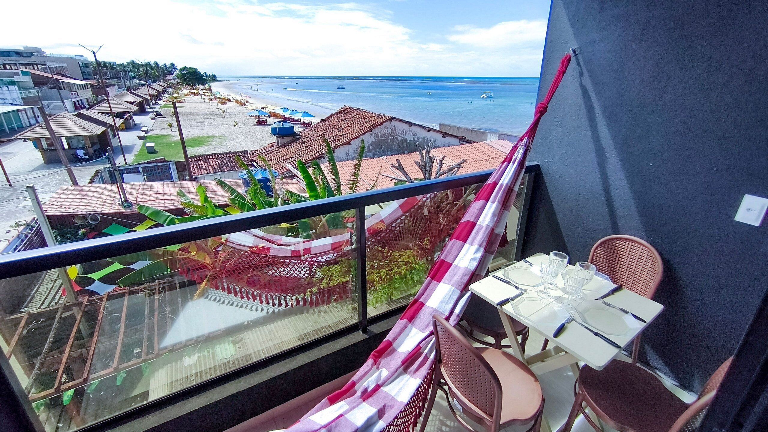 A balcony with a table and chairs, overlooking a beach and buildings.