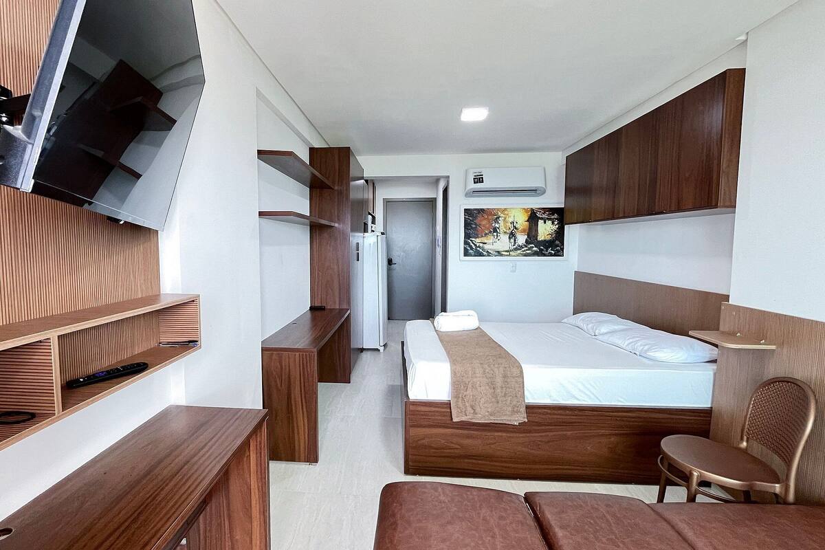 A modern hotel room with a bed, wooden furniture, a TV mounted on the wall, and a painting on the wall.