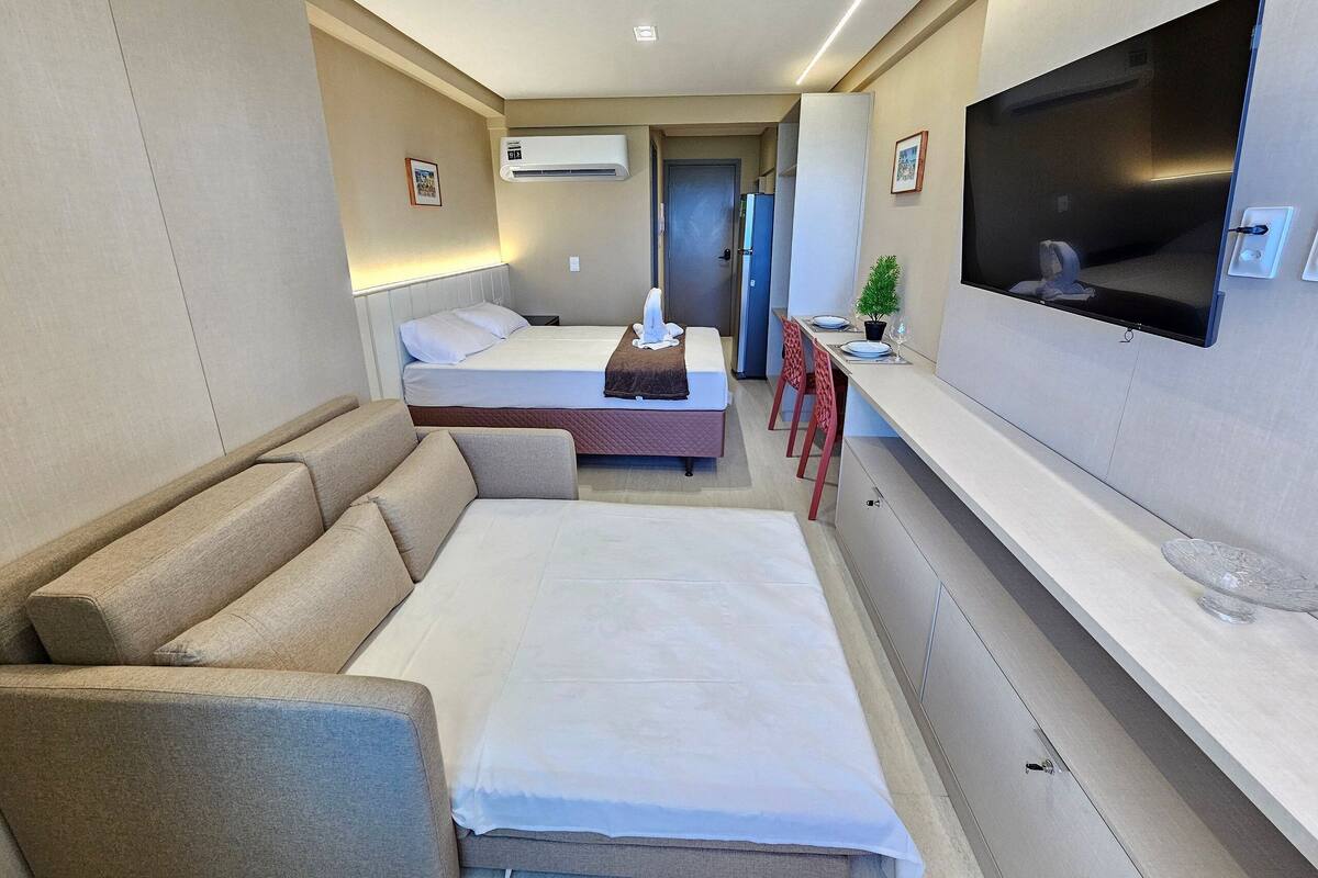 A modern hotel room with a sofa, a bed, a TV, and a small dining area.