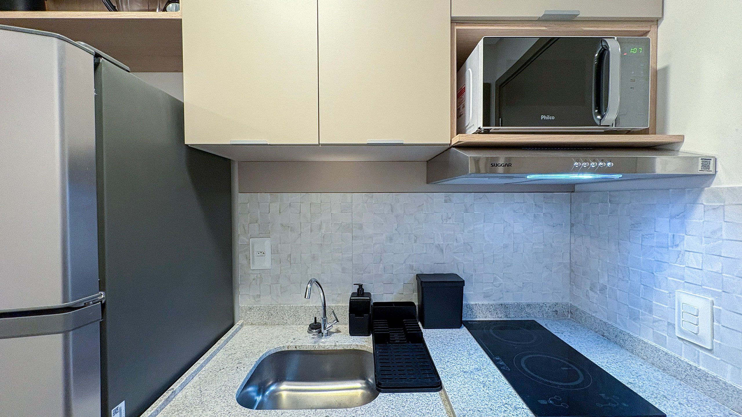 Una cocina compacta con un refrigerador de acero inoxidable, un microondas y un lavabo con un tapete negro.