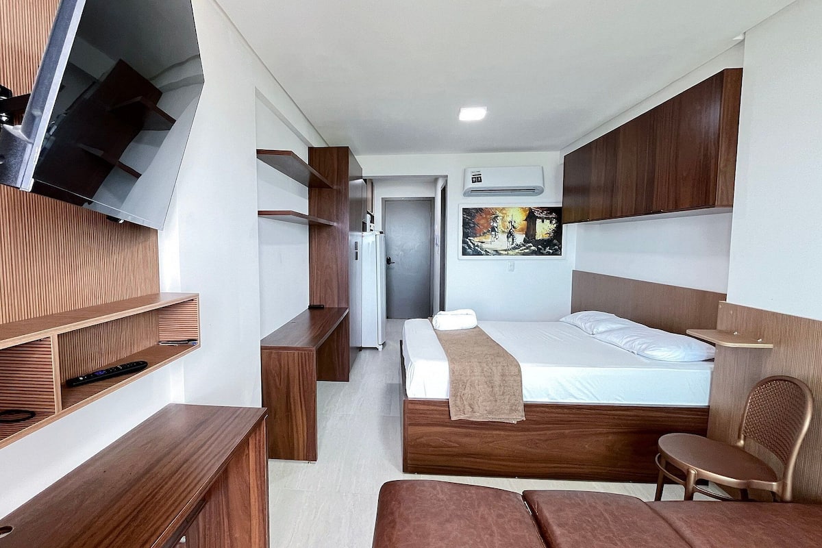 A modern hotel room with a bed, wooden furniture, a TV mounted on the wall, and a painting on the wall.