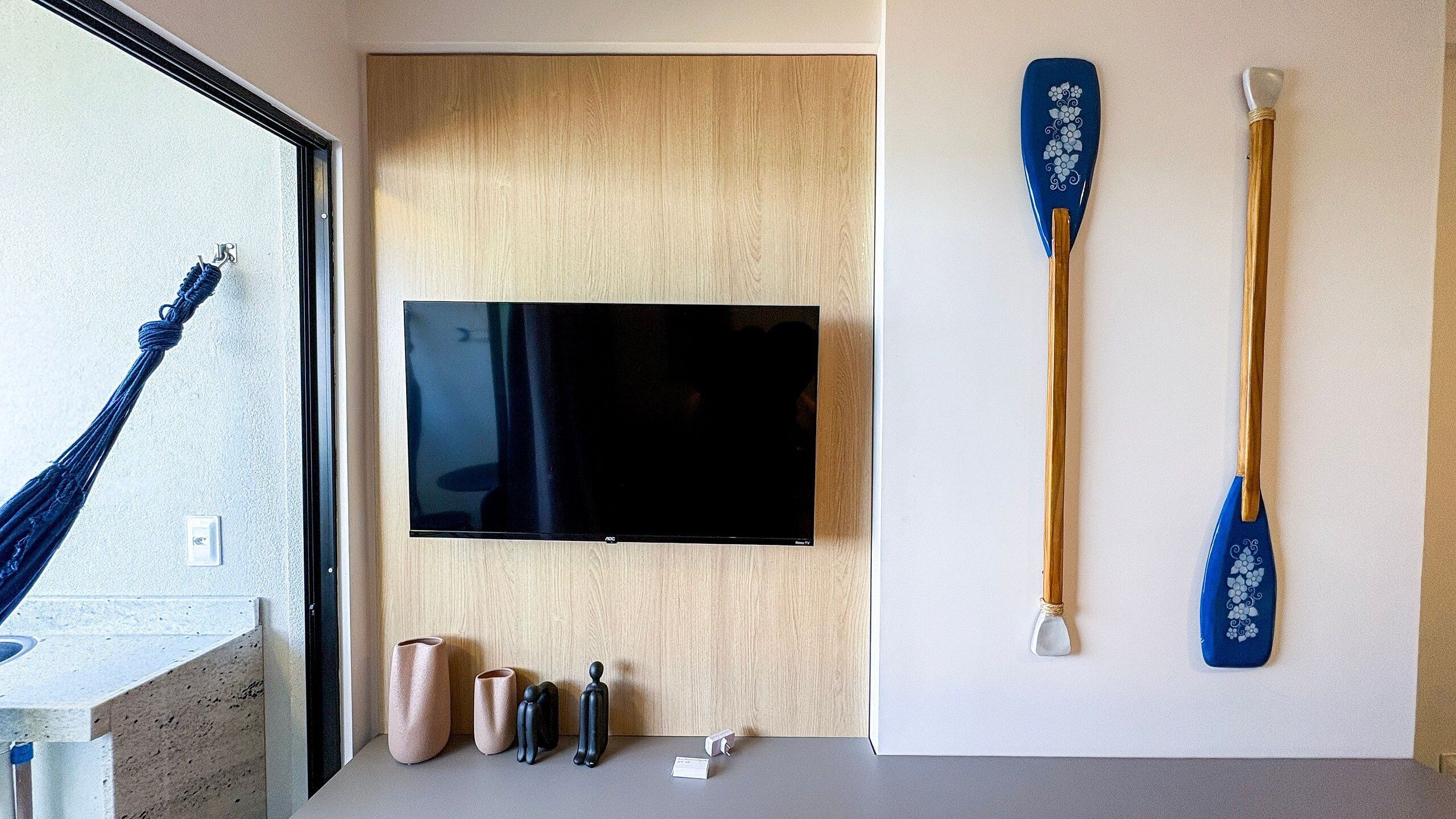 Huoneessa on seinälle asennettu litteänäyttöinen televisio, kaksi sinistä melontamelaa ja puinen ovi.
