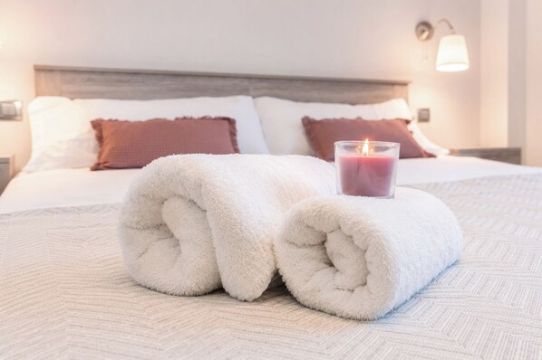 A neatly made bed with rolled white towels and a lit candle, indicating a cozy and well-maintained hotel room.