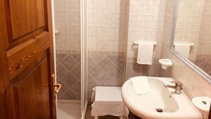 A bathroom with a wooden door, a glass shower enclosure, a sink, and a mirror.