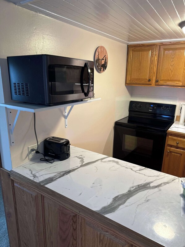 Une cuisine équipée d’un four à micro-ondes, d’un grille-pain, d’une cuisinière et de meubles de rangement en bois.