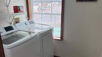 Une buanderie équipée d’un lave-linge et d’un sèche-linge à chargement frontal, d’une fenêtre avec des stores, d’une porte et d’un petit tapis sur le sol.