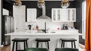 A modern kitchen with a central island, three bar stools, and pendant lighting. - Indy Getaway - Near Downtown Indy - Sleeps 10! (Indianapolis)